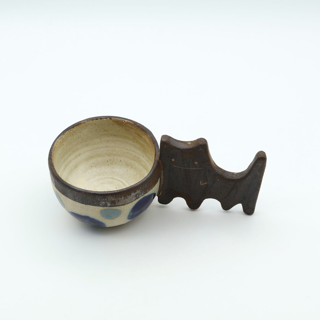 沖縄のやちむん「土の種」によるネコをモチーフにした四つ足カップ。ドット柄のカップに、ネコの体と足を模したユニークな持ち手が組み合わさった、遊び心あふれる陶器のマグカップ。- canosaオンラインショップ