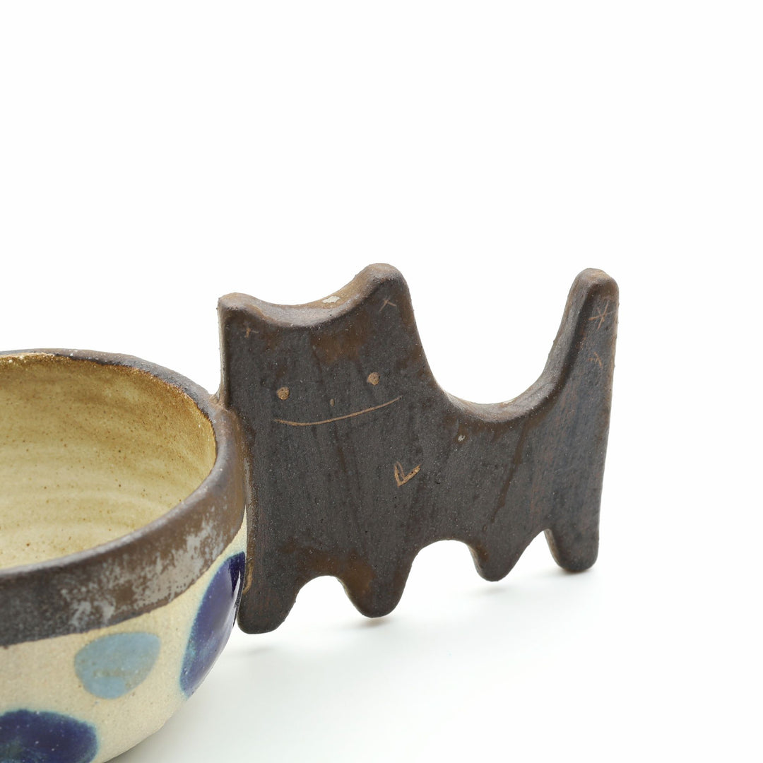 沖縄のやちむん「土の種」によるネコをモチーフにした四つ足カップ。ドット柄のカップに、ネコの体と足を模したユニークな持ち手が組み合わさった、遊び心あふれる陶器のマグカップ。- canosaオンラインショップ