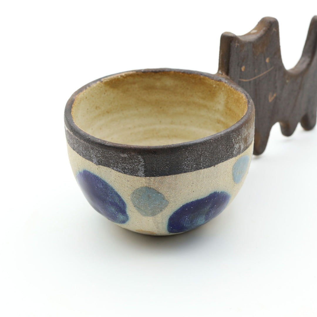 沖縄のやちむん「土の種」によるネコをモチーフにした四つ足カップ。ドット柄のカップに、ネコの体と足を模したユニークな持ち手が組み合わさった、遊び心あふれる陶器のマグカップ。- canosaオンラインショップ