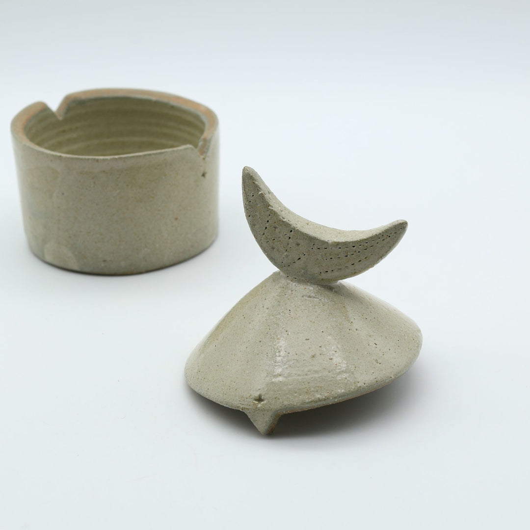 沖縄のやちむん工房「土の種」による素朴な土の質感の陶器の蓋物（キャニスター）。三日月の持ち手と蓋のズレを防ぐ突起が特徴的な、調味料やアクセサリー入れに最適な手仕事のうつわ。