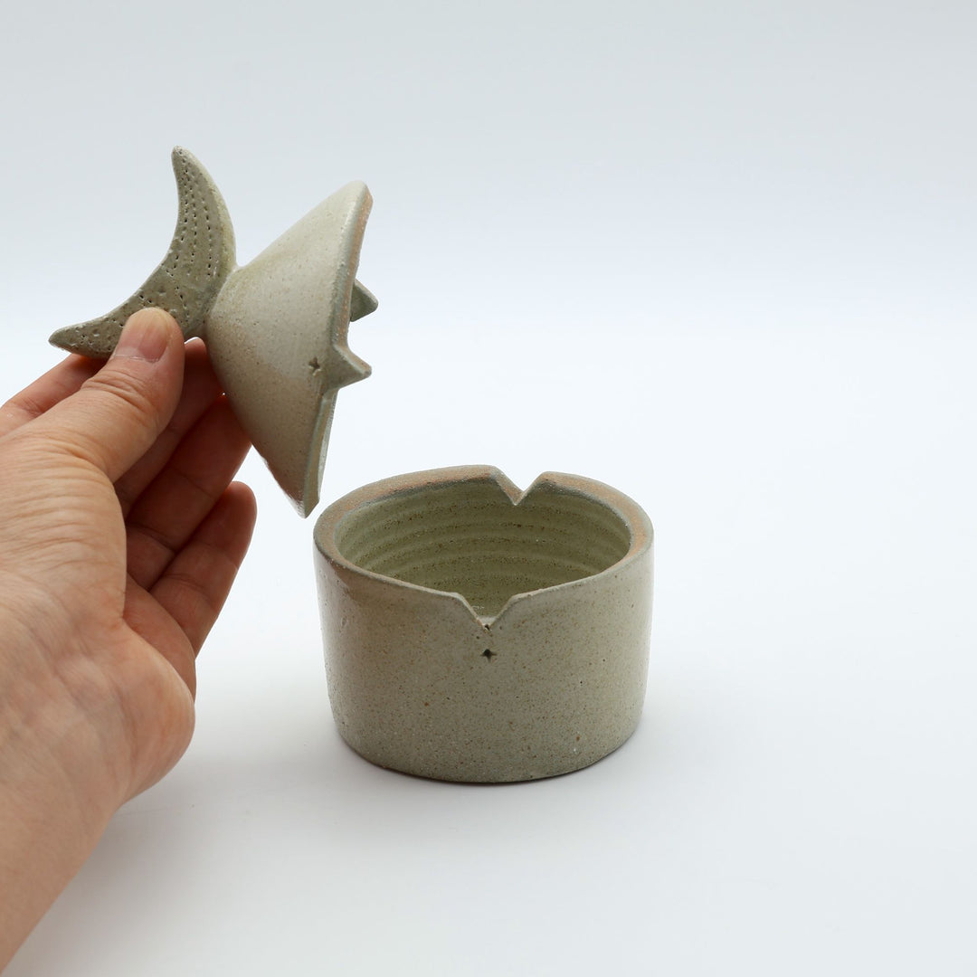 沖縄のやちむん工房「土の種」による素朴な土の質感の陶器の蓋物（キャニスター）。三日月の持ち手と蓋のズレを防ぐ突起が特徴的な、調味料やアクセサリー入れに最適な手仕事のうつわ。