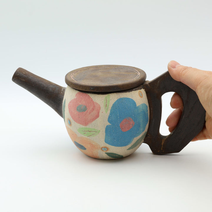 沖縄のやちむん「土の種」によるカラフルな花模様のポット。手描きのアートのような絵付けと、木の枝のような独特な持ち手が特徴的な一点物の器。