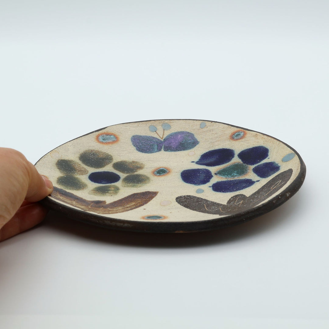 沖縄のやちむん工房「土の種」のサラダ皿。花に舞う蝶や鳥が大胆に絵付けされた手仕事の平皿。