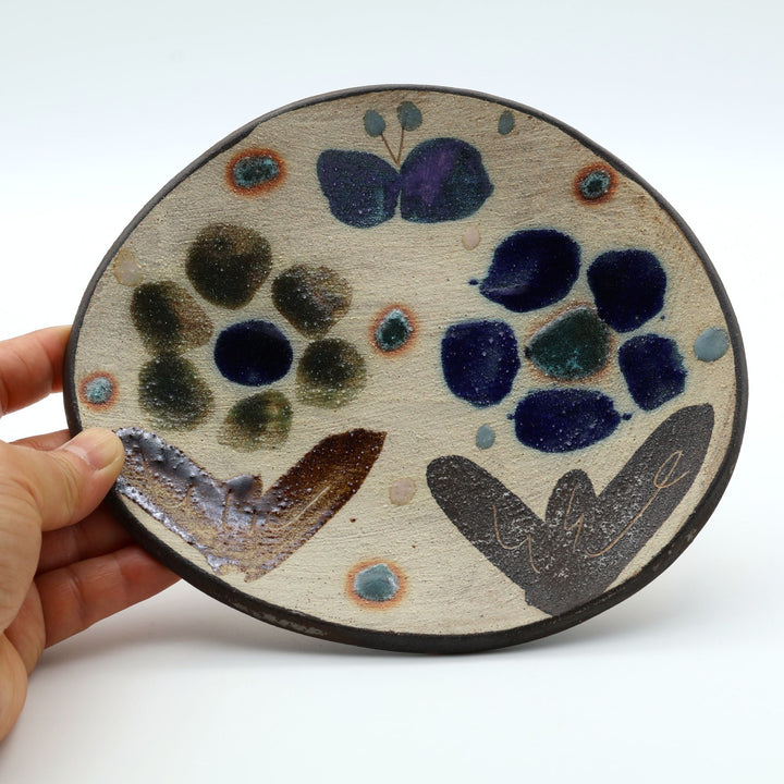 沖縄のやちむん工房「土の種」のサラダ皿。花に舞う蝶や鳥が大胆に絵付けされた手仕事の平皿。