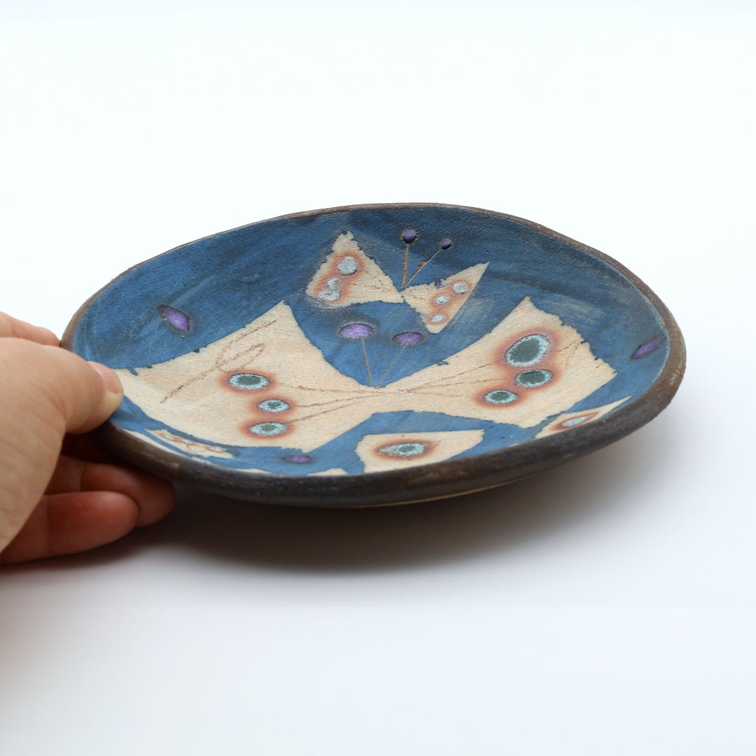沖縄のやちむん工房「土の種」のサラダ皿。鮮やかなコバルトブルーの地色に、蝶が絵付けされた手仕事の平皿。