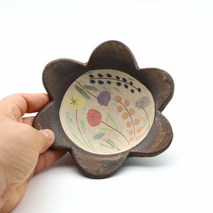 やちむん工房「土の種」の愛らしいふっくらとしたお花型の小鉢。内側に優しく素朴なタッチで植物や小さな花々が絵付けされた、沖縄の手仕事による1点もののうつわ。