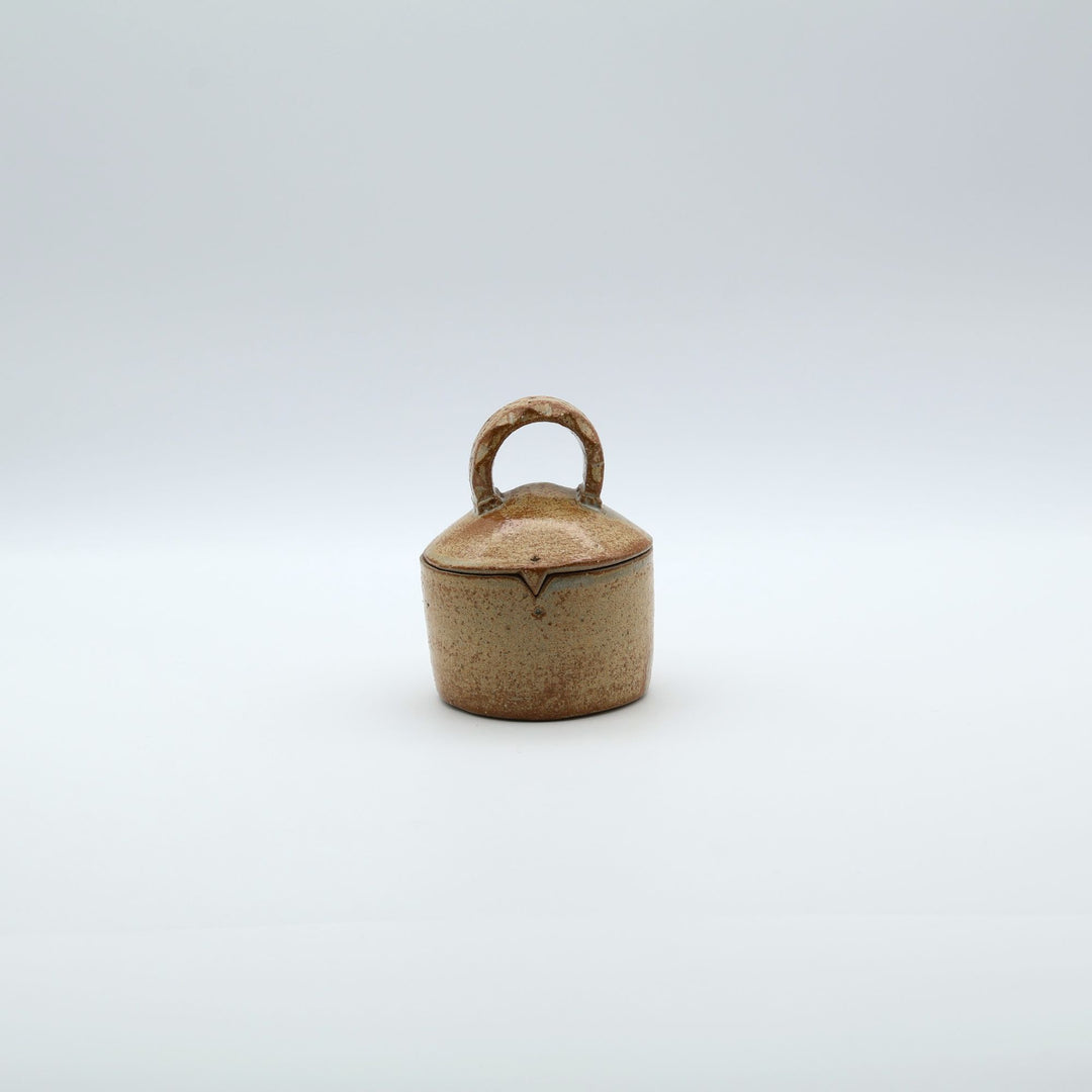 沖縄のやちむん工房「土の種」による素朴な土の質感の陶器の蓋物（キャニスター）。大きな持ち手と蓋のズレを防ぐ突起が特徴的な、調味料やアクセサリー入れに最適な手仕事のうつわ。