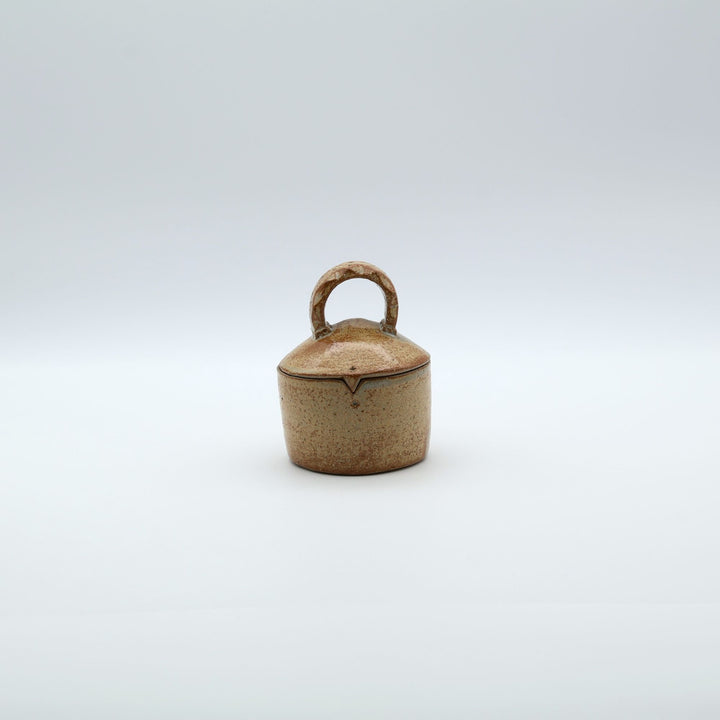 沖縄のやちむん工房「土の種」による素朴な土の質感の陶器の蓋物（キャニスター）。大きな持ち手と蓋のズレを防ぐ突起が特徴的な、調味料やアクセサリー入れに最適な手仕事のうつわ。