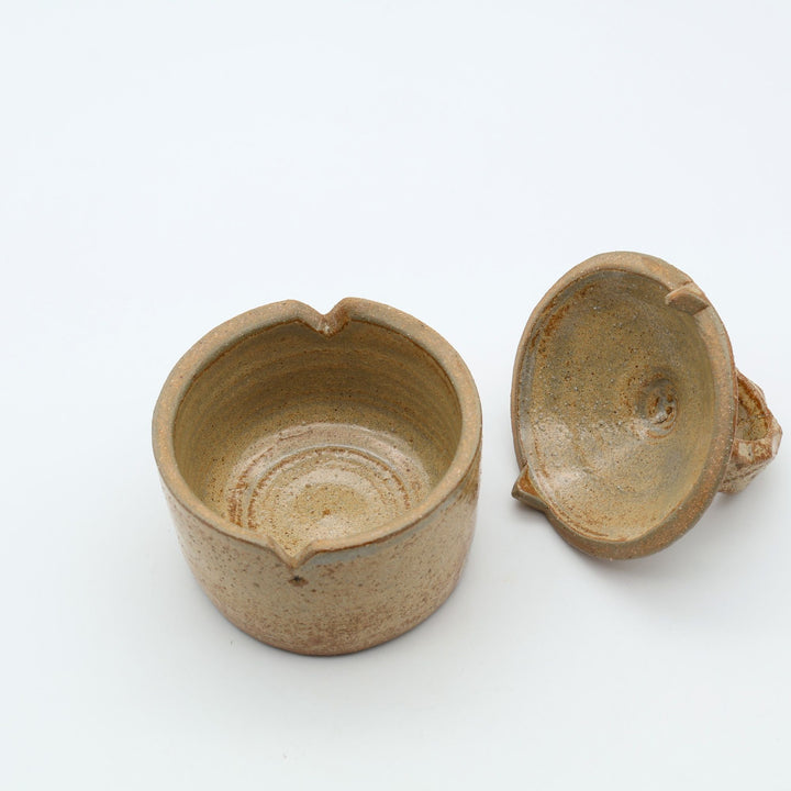 沖縄のやちむん工房「土の種」による素朴な土の質感の陶器の蓋物（キャニスター）。大きな持ち手と蓋のズレを防ぐ突起が特徴的な、調味料やアクセサリー入れに最適な手仕事のうつわ。