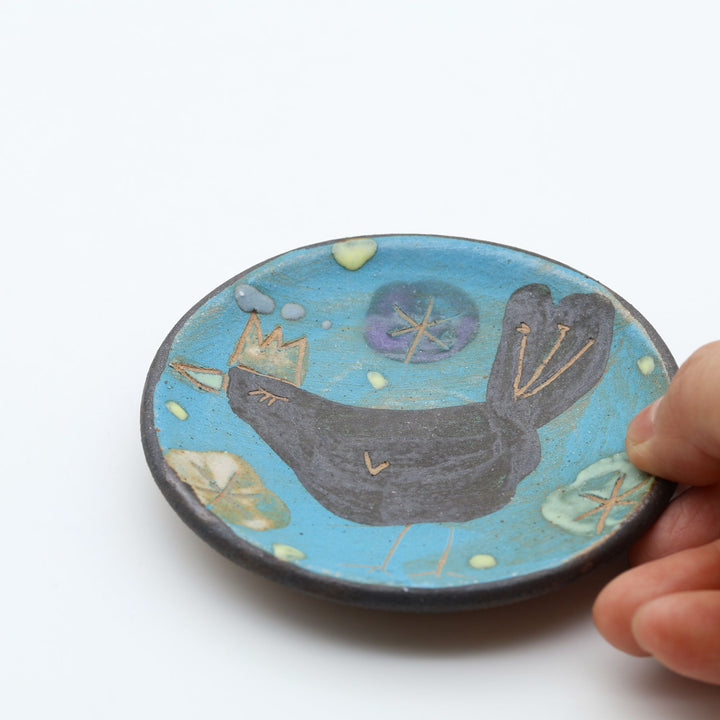 土の種（沖縄県うるま市）作、鮮やかなブルー地に王冠をかぶった鳥が描かれた手描き陶器豆皿。やちむんの器。