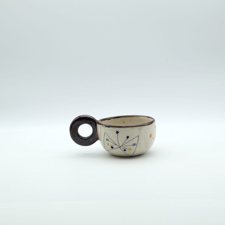 うるま市のやちむん工房「土の種」作、外側にお花と蝶々（ちょうちょ）が描かれた粉引きマグカップ。丸い茶色のリング型持ち手が特徴。/ Handcrafted Kohiki ceramic mug with whimsical flower and butterfly illustrations and a distinct circular handle by Tsuchi no Tane, Okinawa.