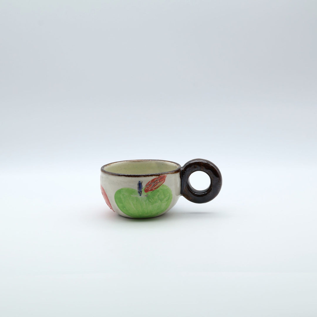 沖縄の陶器「土の種」のリンゴ柄粉引マグカップ。外側に並ぶ3色のリンゴと、内側にワンポイントで描かれた青リンゴ。/ Artisan Okinawan pottery mug by Tsuchi no Tane, showing the colorful apple motifs on the outside and a single green apple painted inside.