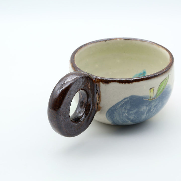 沖縄の陶器「土の種」のリンゴ柄粉引マグカップ。外側に並ぶ3色のリンゴと、内側にワンポイントで描かれた青リンゴ。/ Artisan Okinawan pottery mug by Tsuchi no Tane, showing the colorful apple motifs on the outside and a single green apple painted inside.