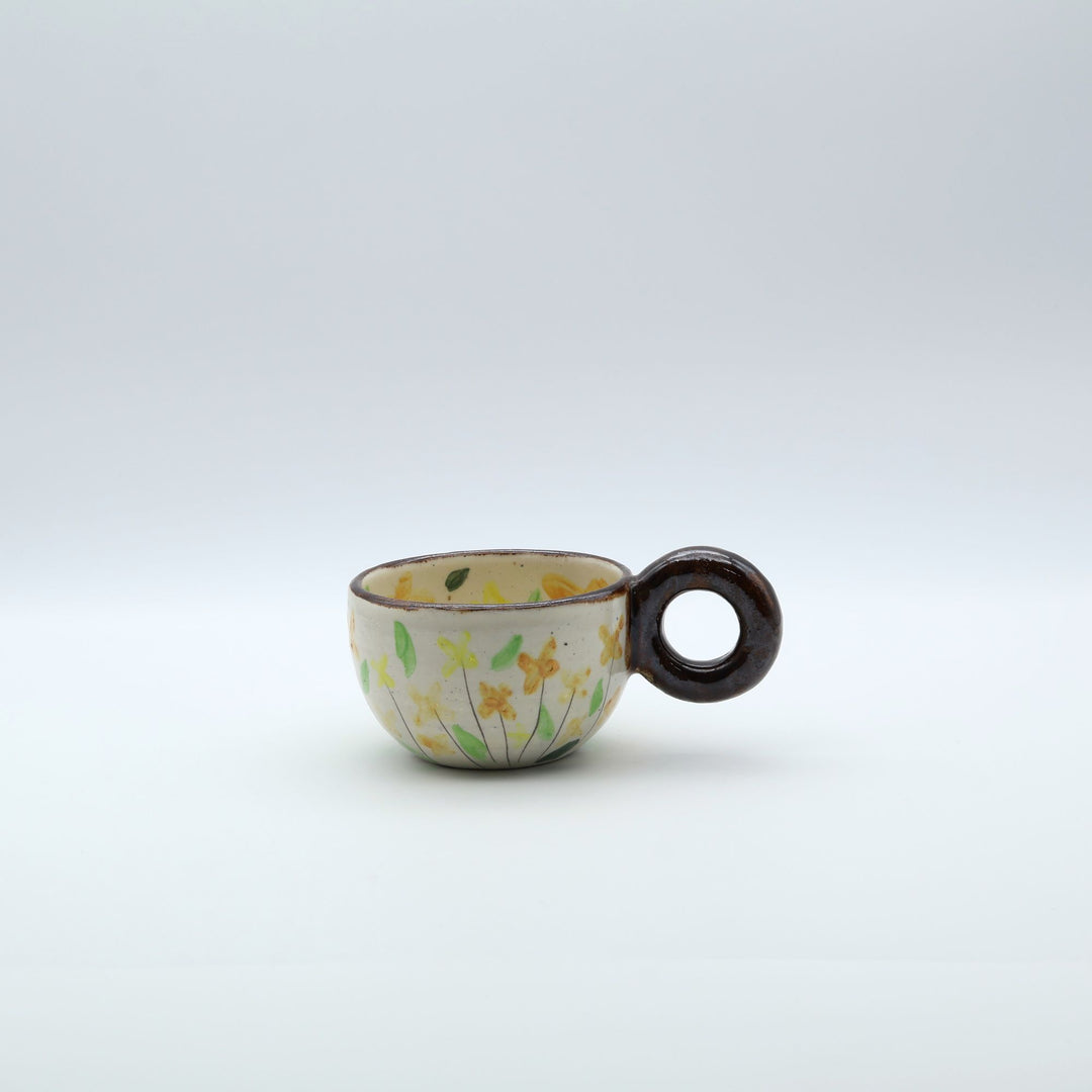 うるま市のやちむん工房「土の種」作、可愛い黄色いお花が描かれた粉引きのマグカップ。特徴的な丸い茶色のリング型持ち手。/ Handcrafted white ceramic mug with yellow and orange floral illustrations and a distinct brown circular handle by Tsuchi no Tane, Okinawa.