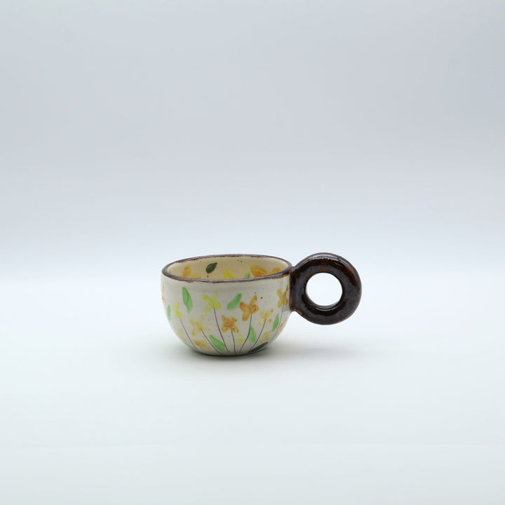 うるま市のやちむん工房「土の種」作、可愛い黄色いお花が描かれた粉引きのマグカップ。特徴的な丸い茶色のリング型持ち手。/ Handcrafted white ceramic mug with yellow and orange floral illustrations and a distinct brown circular handle by Tsuchi no Tane, Okinawa.