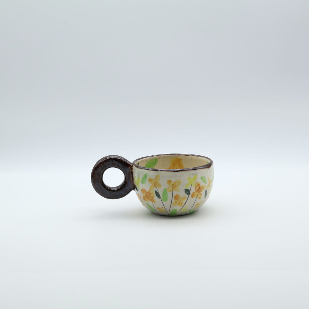 うるま市のやちむん工房「土の種」作、可愛い黄色いお花が描かれた粉引きのマグカップ。特徴的な丸い茶色のリング型持ち手。/ Handcrafted white ceramic mug with yellow and orange floral illustrations and a distinct brown circular handle by Tsuchi no Tane, Okinawa.