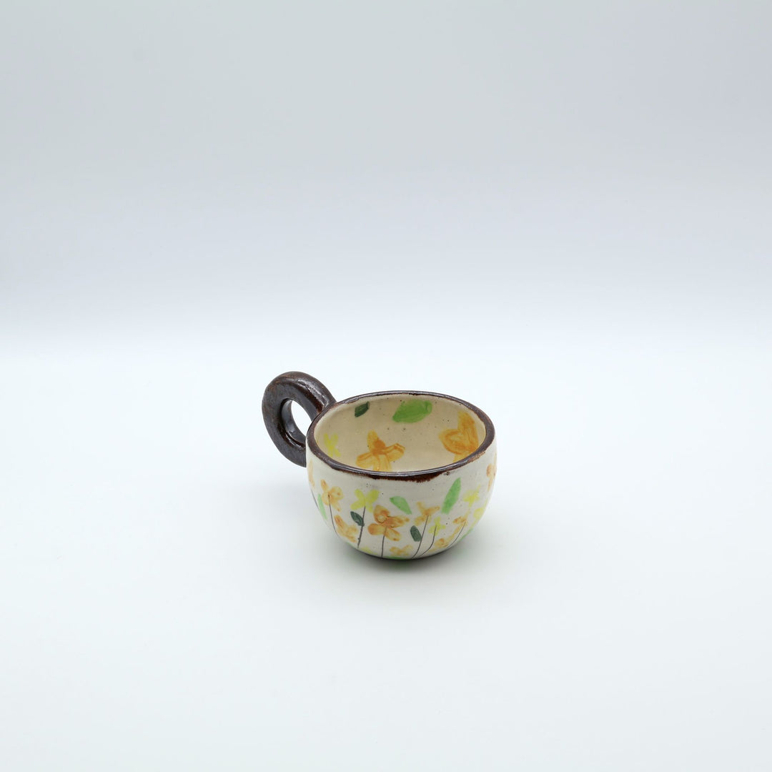 うるま市のやちむん工房「土の種」作、可愛い黄色いお花が描かれた粉引きのマグカップ。特徴的な丸い茶色のリング型持ち手。/ Handcrafted white ceramic mug with yellow and orange floral illustrations and a distinct brown ring handle by Tsuchi no Tane, Okinawa.