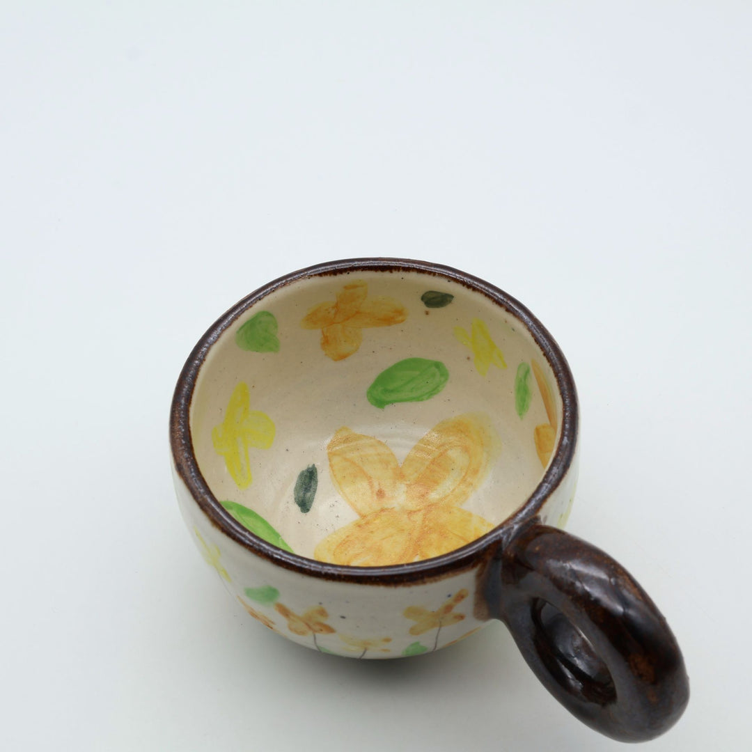 うるま市のやちむん工房「土の種」作、可愛い黄色いお花が描かれた粉引きのマグカップ。特徴的な丸い茶色のリング型持ち手。/ Handcrafted white ceramic mug with yellow and orange floral illustrations and a distinct brown circular handle by Tsuchi no Tane, Okinawa.