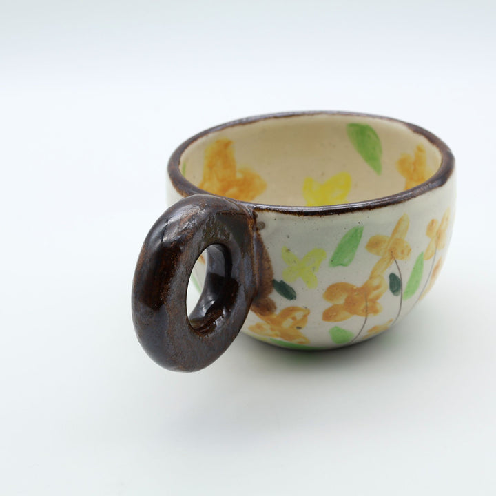 うるま市のやちむん工房「土の種」作、可愛い黄色いお花が描かれた粉引きのマグカップ。特徴的な丸い茶色のリング型持ち手。/ Handcrafted white ceramic mug with yellow and orange floral illustrations and a distinct brown ring handle by Tsuchi no Tane, Okinawa.