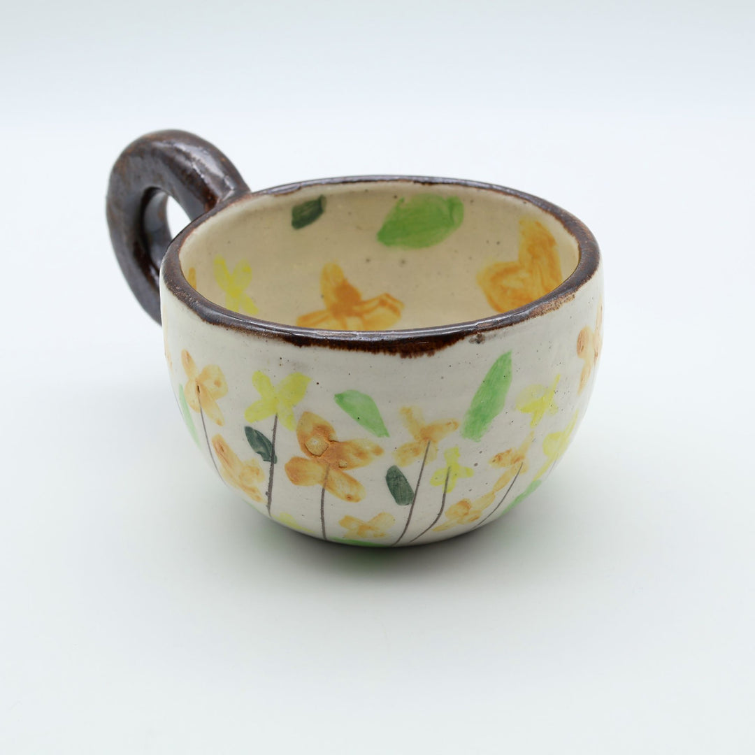 うるま市のやちむん工房「土の種」作、可愛い黄色いお花が描かれた粉引きのマグカップ。特徴的な丸い茶色のリング型持ち手。/ Handcrafted white ceramic mug with yellow and orange floral illustrations and a distinct brown circular handle by Tsuchi no Tane, Okinawa.