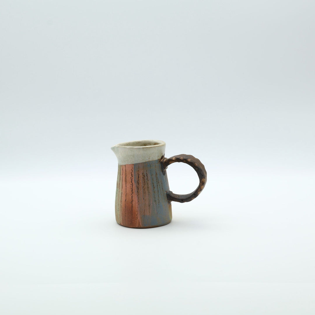 うるま市のやちむん工房「土の種」作、白化粧と虹色のグラデーションが美しい陶器のピッチャー。手彫りのギザギザとした彫理が施された持ち手。/ Close-up of a handcrafted Okinawan Yachumun ceramic pitcher by Tsuchi no Tane, featuring a hand-carved textured handle and intricate glaze work.