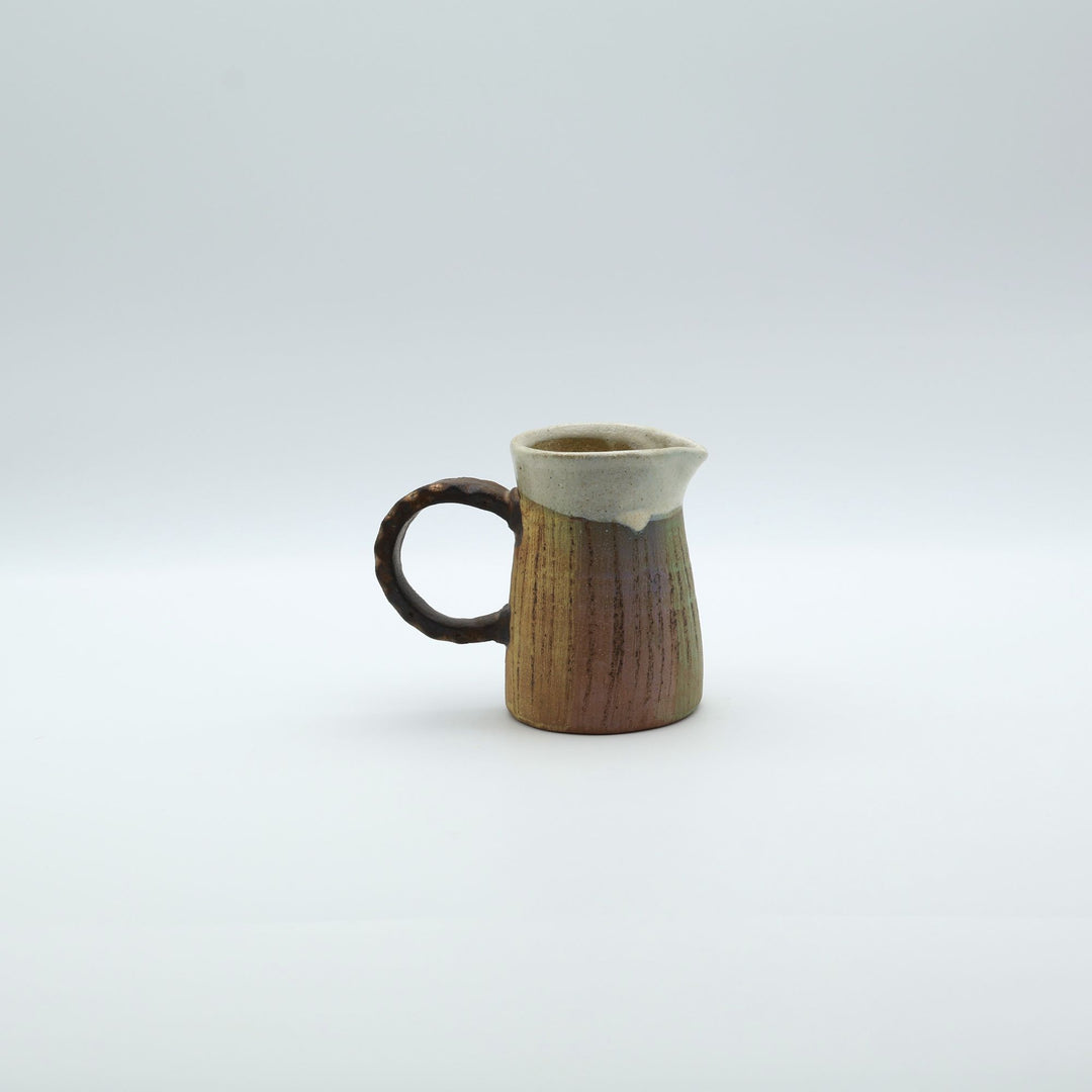 うるま市のやちむん工房「土の種」作、白化粧と虹色のグラデーションが美しい陶器のピッチャー。手彫りのギザギザとした彫理が施された持ち手。/ Close-up of a handcrafted Okinawan Yachumun ceramic pitcher by Tsuchi no Tane, featuring a hand-carved textured handle and intricate glaze work.