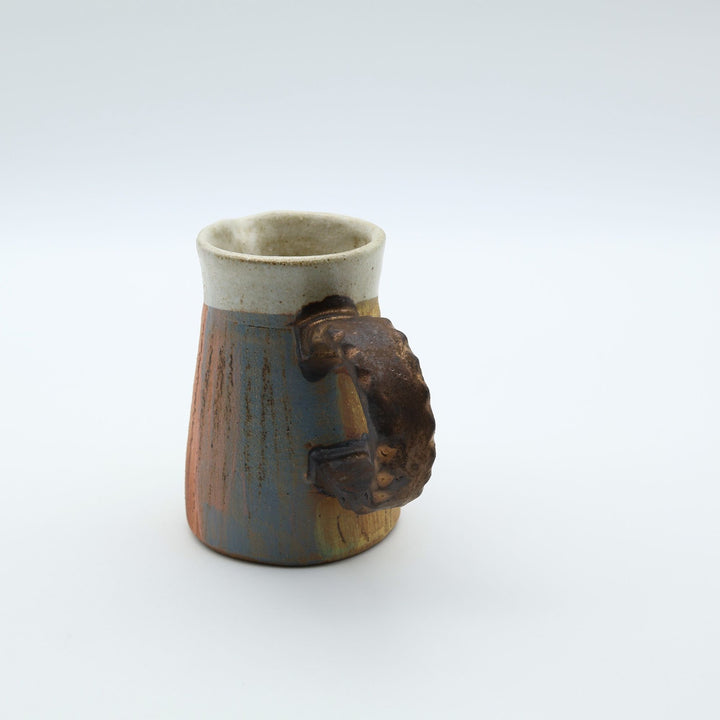 うるま市のやちむん工房「土の種」作、白化粧と虹色のグラデーションが美しい陶器のピッチャー。手彫りのギザギザとした彫理が施された持ち手。/ Close-up of a handcrafted Okinawan Yachumun ceramic pitcher by Tsuchi no Tane, featuring a hand-carved textured handle and intricate glaze work.