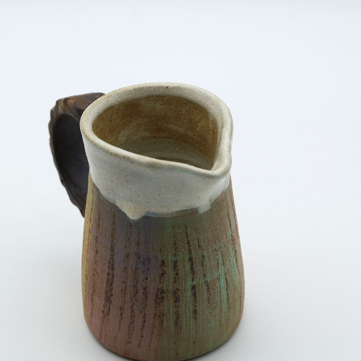 うるま市のやちむん工房「土の種」作、白化粧と虹色のグラデーションが美しい陶器のピッチャー。手彫りのギザギザとした彫理が施された持ち手。/ Close-up of a handcrafted Okinawan Yachumun ceramic pitcher by Tsuchi no Tane, featuring a hand-carved textured handle and intricate glaze work.