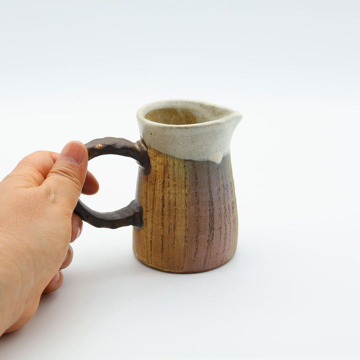 うるま市のやちむん工房「土の種」作、白化粧と虹色のグラデーションが美しい陶器のピッチャー。手彫りのギザギザとした彫理が施された持ち手。/ Close-up of a handcrafted Okinawan Yachumun ceramic pitcher by Tsuchi no Tane, featuring a hand-carved textured handle and intricate glaze work.