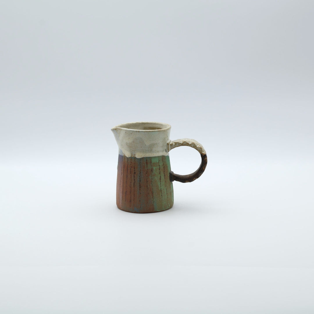 うるま市のやちむん工房「土の種」作、白化粧と虹色のグラデーションが美しい陶器のピッチャー。手彫りのギザギザとした彫理が施された持ち手。/ Close-up of a handcrafted Okinawan Yachumun ceramic pitcher by Tsuchi no Tane, featuring a hand-carved textured handle and intricate glaze work.
