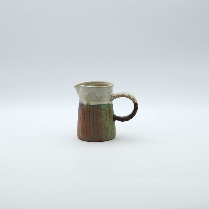 うるま市のやちむん工房「土の種」作、白化粧と虹色のグラデーションが美しい陶器のピッチャー。手彫りのギザギザとした彫理が施された持ち手。/ Close-up of a handcrafted Okinawan Yachumun ceramic pitcher by Tsuchi no Tane, featuring a hand-carved textured handle and intricate glaze work.