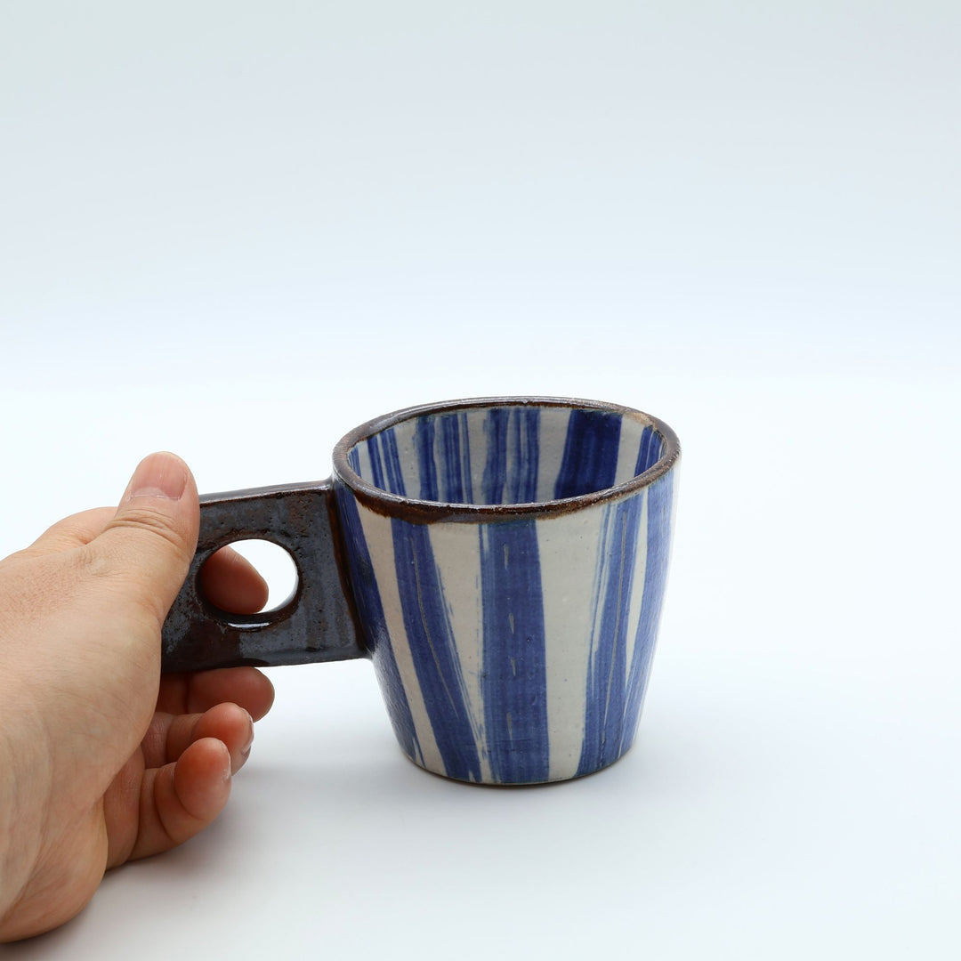 沖縄のやちむん作家「土の種」による、白と青のランダムなストライプ柄が爽やかな1点ものの小ぶりなマグカップ。四角い板状の持ち手に丸い穴がくり抜かれたユニークなデザイン。