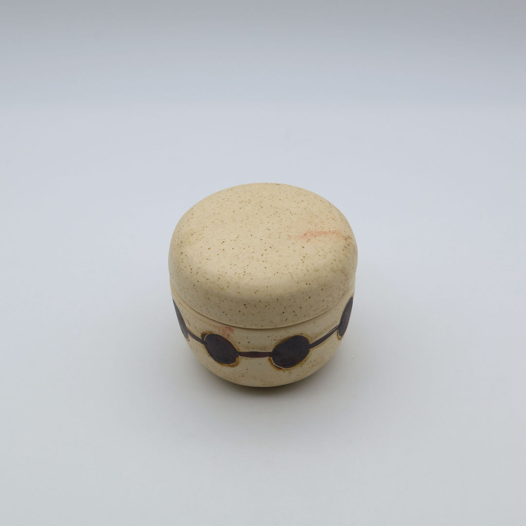 sora potters workによる、温かみのあるベージュの器肌に丸と線の模様が描かれた、蓋が添えられたやちむんの蓋物（キャニスター）