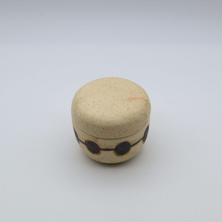 sora potters workによる、温かみのあるベージュの器肌に丸と線の模様が描かれた、蓋が添えられたやちむんの蓋物（キャニスター）