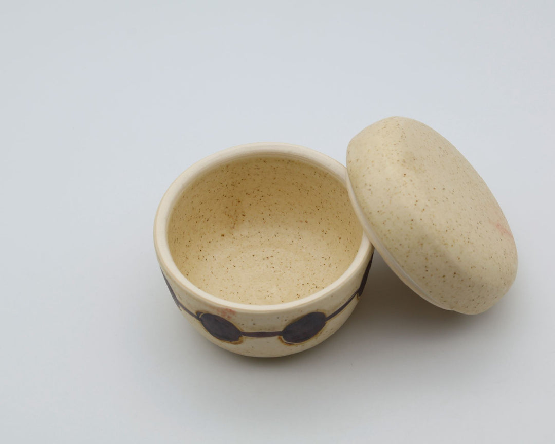 sora potters workによる、温かみのあるベージュの器肌に丸と線の模様が描かれた、蓋が添えられたやちむんの蓋物（キャニスター）
