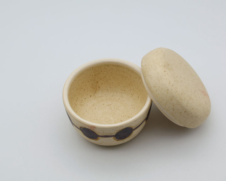 sora potters workによる、温かみのあるベージュの器肌に丸と線の模様が描かれた、蓋が添えられたやちむんの蓋物（キャニスター）