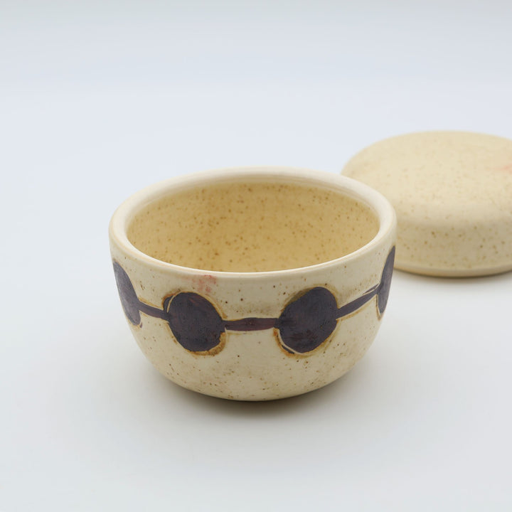 sora potters workによる、温かみのあるベージュの器肌に丸と線の模様が描かれた、蓋が添えられたやちむんの蓋物（キャニスター）