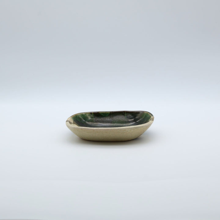 宋艸窯（そうそうがま）が異なる色の粘土を組み合わせて作った、練り込み技法に緑釉を半分に掛け分けた長方形の小皿。緑と白背景の中央に置かれた、モダンな幾何学模様と丸みのあるフォルムが美しい手仕事の豆皿です。
