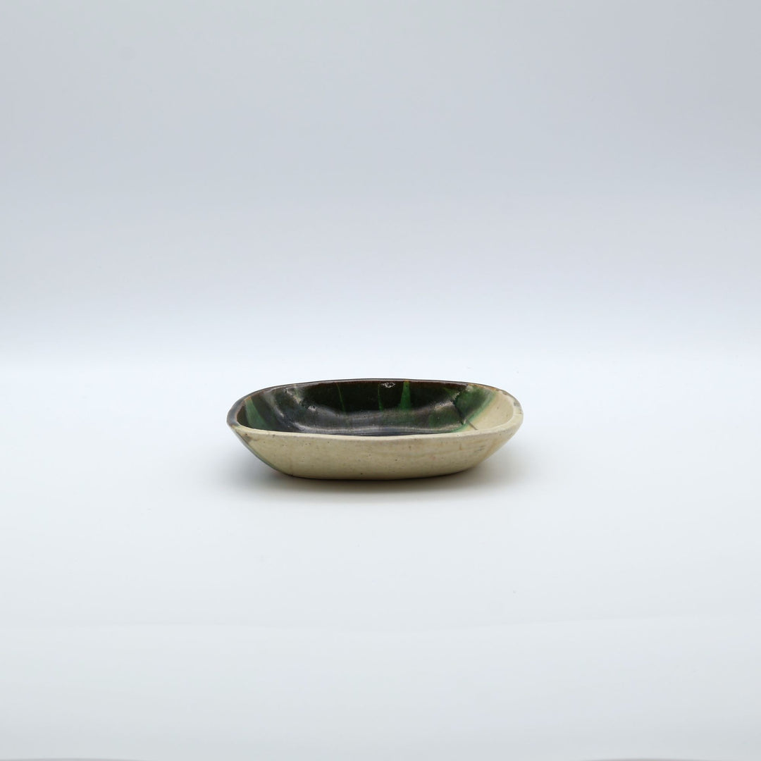 宋艸窯（そうそうがま）が異なる色の粘土を組み合わせて作った、練り込み技法に緑釉を斜め半分に掛け分けた長方形の小皿。緑と白背景の中央に置かれた、モダンな幾何学模様と丸みのあるフォルムが美しい手仕事の豆皿です。