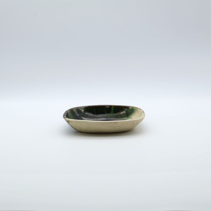 宋艸窯（そうそうがま）が異なる色の粘土を組み合わせて作った、練り込み技法に緑釉を斜め半分に掛け分けた長方形の小皿。緑と白背景の中央に置かれた、モダンな幾何学模様と丸みのあるフォルムが美しい手仕事の豆皿です。