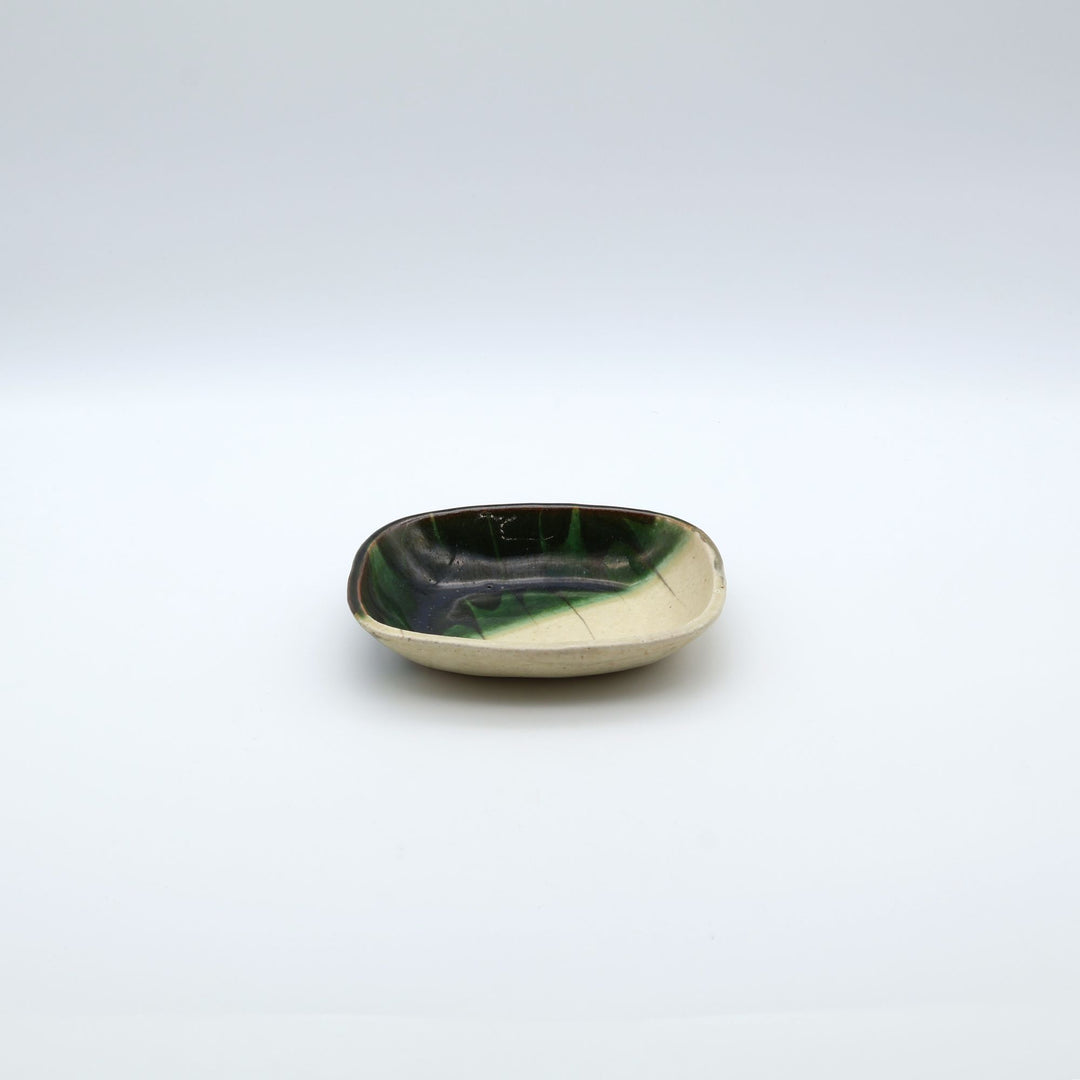 宋艸窯（そうそうがま）が異なる色の粘土を組み合わせて作った、練り込み技法に緑釉を斜め半分に掛け分けた長方形の小皿。緑と白背景の中央に置かれた、モダンな幾何学模様と丸みのあるフォルムが美しい手仕事の豆皿です。