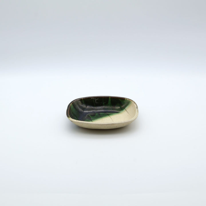 宋艸窯（そうそうがま）が異なる色の粘土を組み合わせて作った、練り込み技法に緑釉を斜め半分に掛け分けた長方形の小皿。緑と白背景の中央に置かれた、モダンな幾何学模様と丸みのあるフォルムが美しい手仕事の豆皿です。