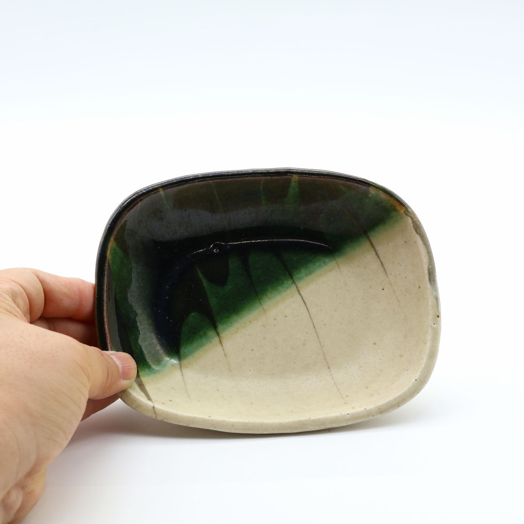 宋艸窯（そうそうがま）が異なる色の粘土を組み合わせて作った、練り込み技法に緑釉を斜め半分に掛け分けた長方形の小皿。緑と白背景の中央に置かれた、モダンな幾何学模様と丸みのあるフォルムが美しい手仕事の豆皿です。