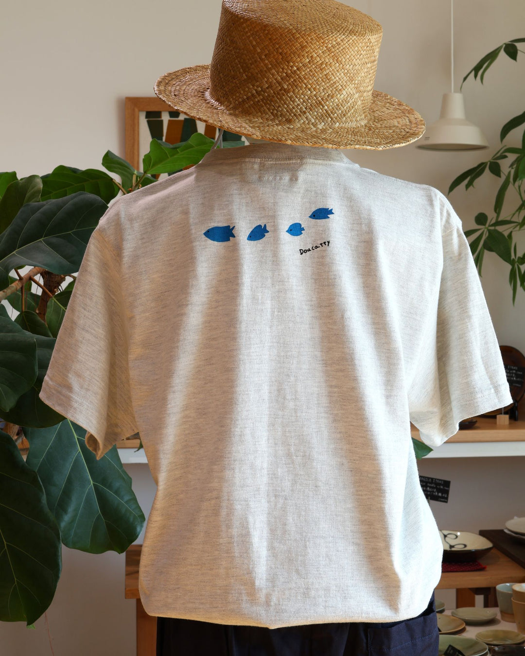 Doucatty（ドゥカティ）の手捺染Tシャツ「ダツくん」の背面。肩のあたりに、鮮やかな青色で描かれた小さな魚3匹が右に向かって並んで泳ぐ姿と「Doucatty」の手書きロゴがプリントされている。沖縄製。