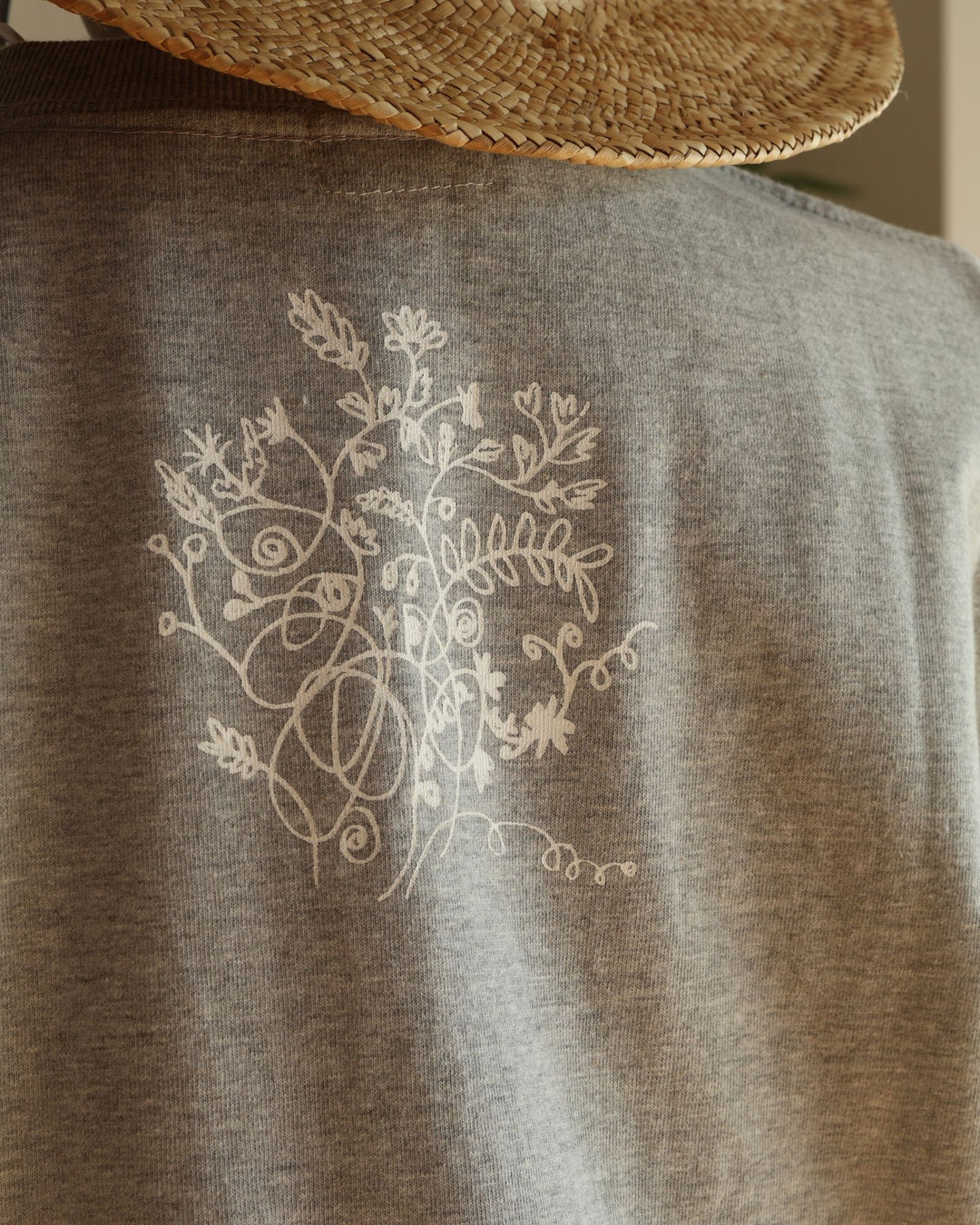 Doucatty（ドゥカティ）の手捺染Tシャツ「ヤギのメリー」のバックプリント。首元下の中央に、繊細な白の線画で繊細に描かれた上品な草花（ボタニカルモチーフ）のイラストが施されている。