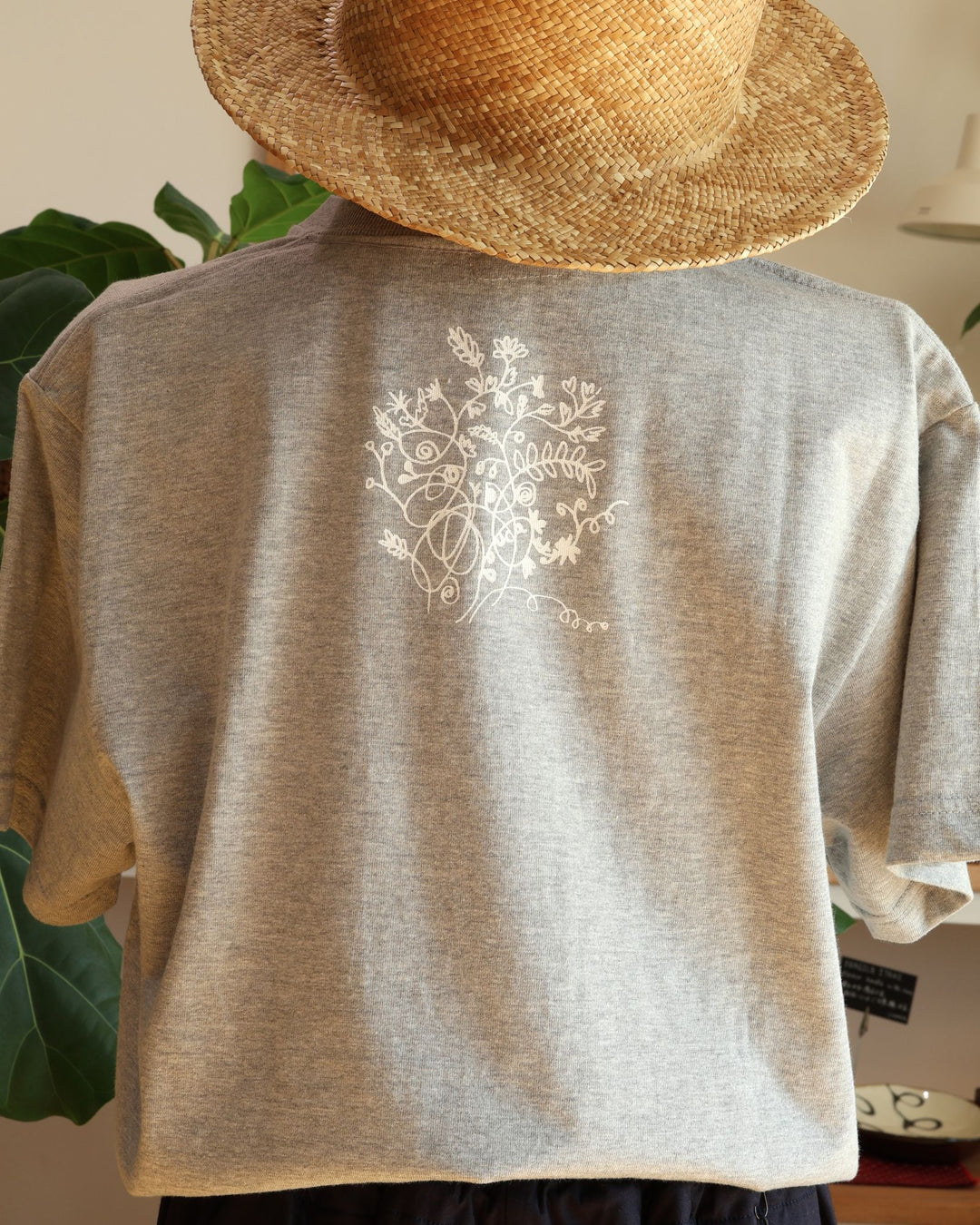 Doucatty（ドゥカティ）の手捺染Tシャツ「ヤギのメリー」のバックプリント。首元下の中央に、繊細な白の線画で繊細に描かれた上品な草花（ボタニカルモチーフ）のイラストが施されている。