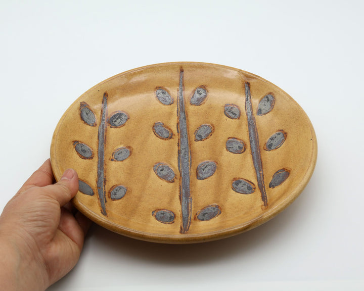 沖縄のやちむん（暮らしの器）。ベージュ・はちみつ色の優しい色合いに、草木模様が施されたシンプルな7寸皿。主菜やワンプレートに活躍する厚みのある丸皿。