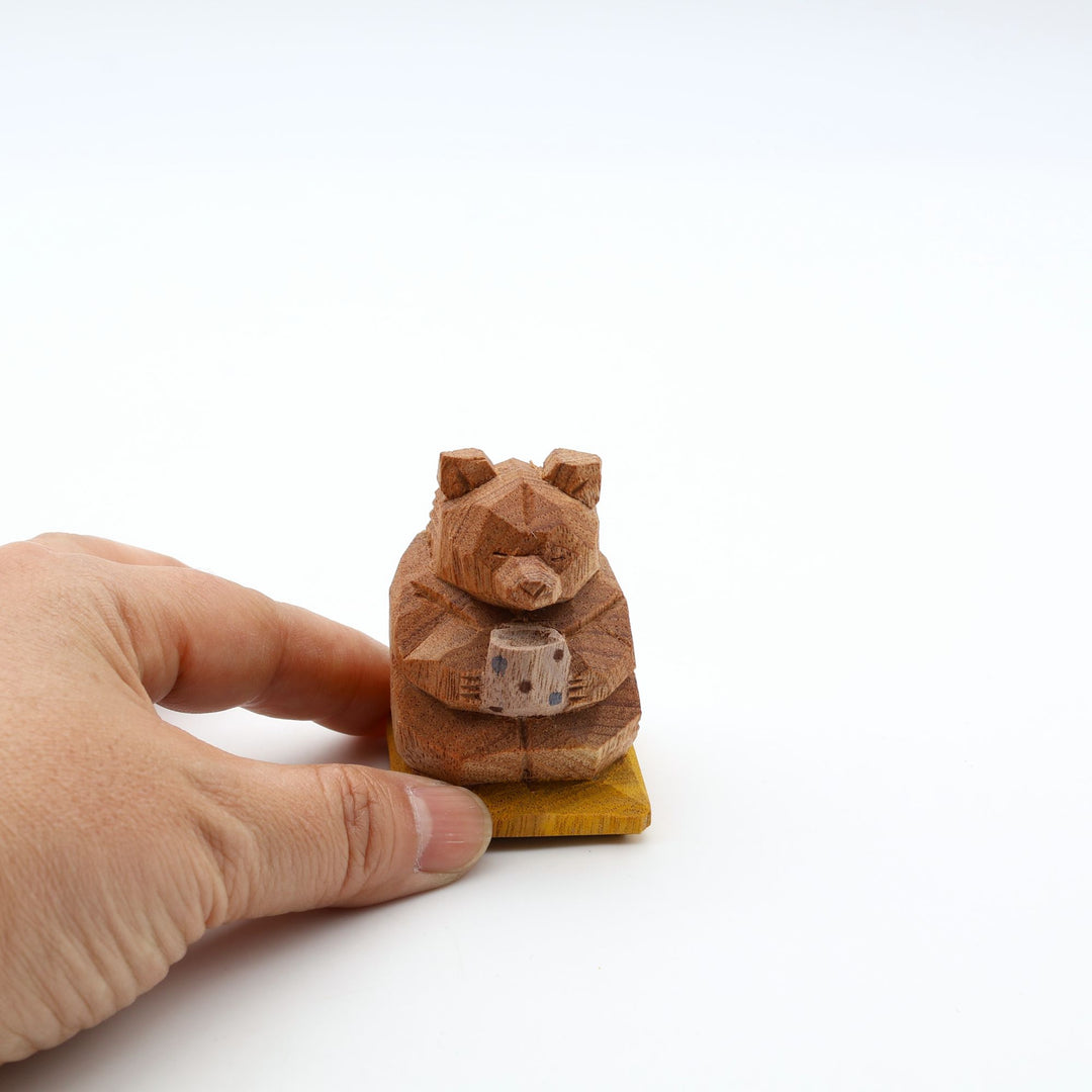 岐阜の木彫り熊作家「gizakuma」が彫る、大切そうに「やちむん」の湯呑みでお茶を飲んでいる「くま」。座布団の上でほっと一息ついてリラックスしている手彫りの木製オブジェ。